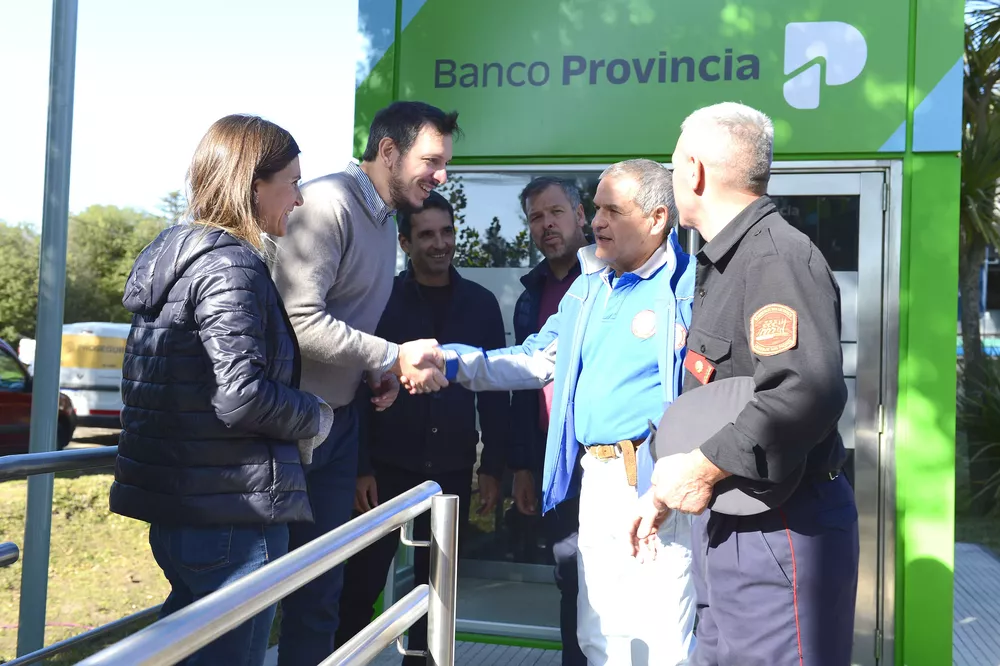 Juan Cuattromo y Fernanda Raverta conversando con dos bomberos voluntarios de Sierra de los Padres durante la inauguración de una cabina de cajeros en esa localidad marplatense